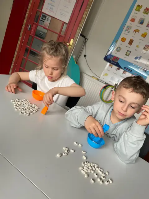 Dzieci zbierają fasolę z literami kolorowymi łyżeczkami