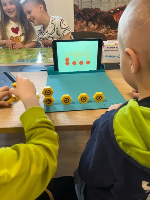 Dzieci układają żółte klocki heksagonalne przy tablecie Plugo