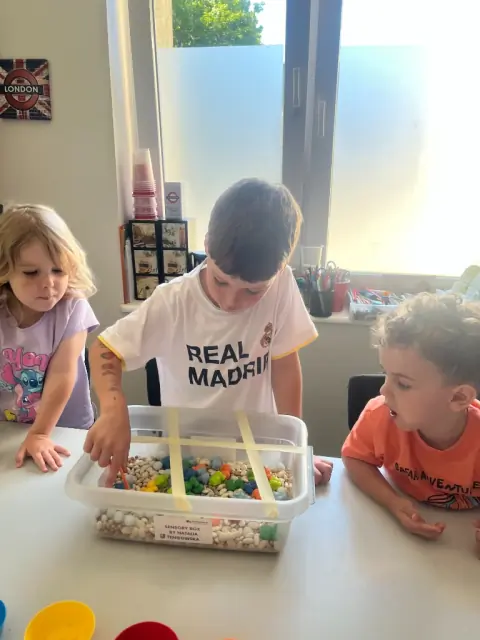 Dzieci sięgają do Sensory Box przez siatkę z taśmy