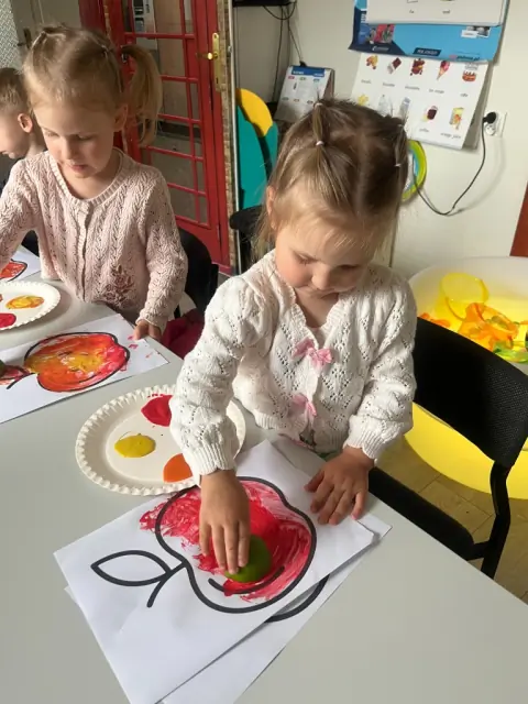 Dziewczynka stempluje jabłko połówką limonki i farbą