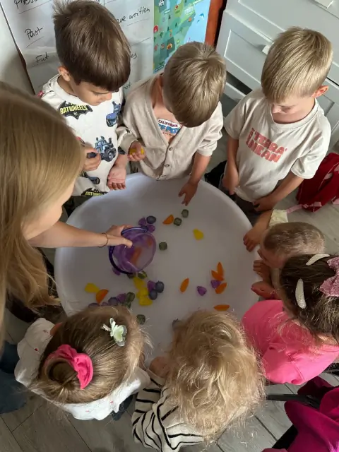Nauczycielka i dzieci przy misce z wodą i owocami