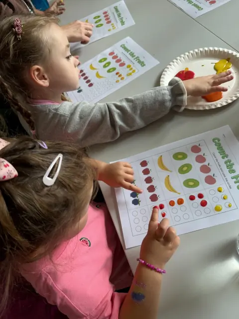 Dziewczynki malują palcami kartę Count the Fruits
